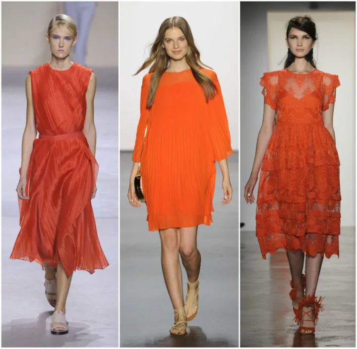 Three models walking down the runway wearing different styles and shades of orange at a fashion event.